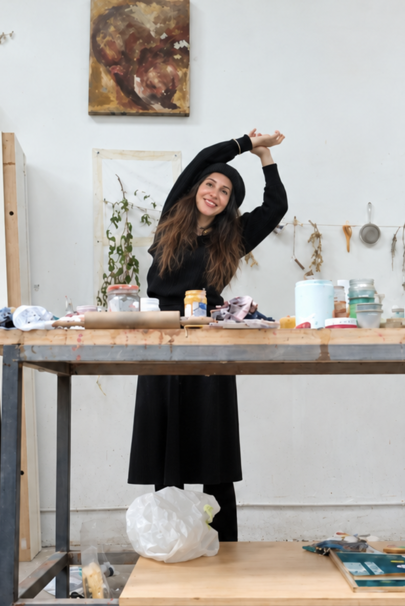 Maya Segarra Terrazas in her studio with arms raised, surrounded by materials and work-in-progress